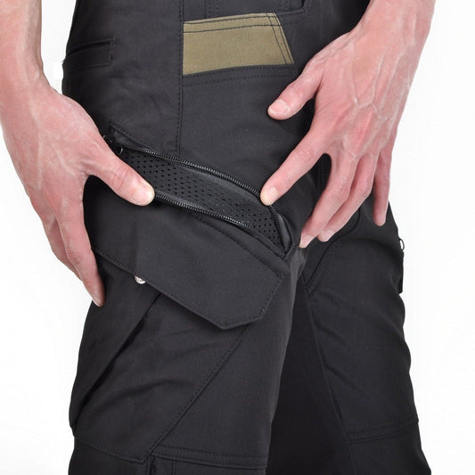 Hands pulling open a zipped mesh vent panel on the thigh of black cargo riding trousers, above a flap pocket with a press stud, on a white background