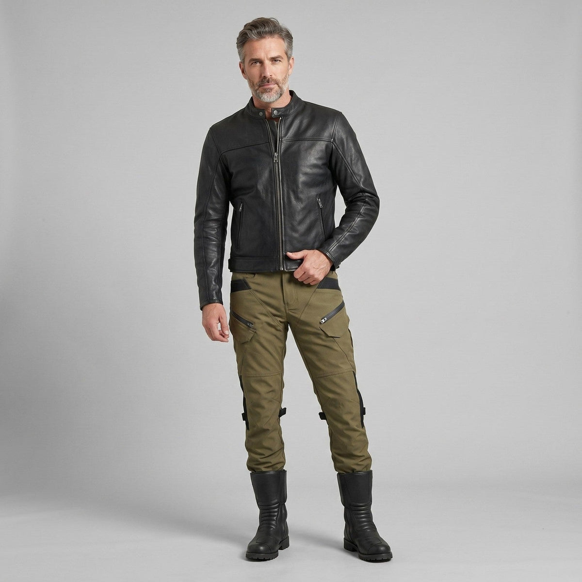 Rider in a black jacket and olive green NORDRYK RoadVault cargo motorcycle trousers standing in a grey studio setting
