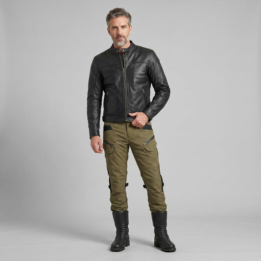 Rider in a black jacket and olive green NORDRYK RoadVault cargo motorcycle trousers standing in a grey studio setting