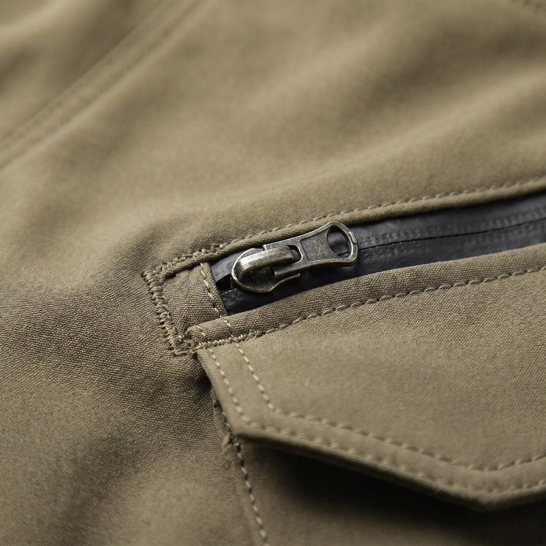 Close-up of olive NORDRYK RoadVault trouser fabric with double stitching and a zipped pocket under a flap